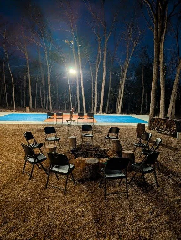 Fire pit circle with chairs at night, lit court in background