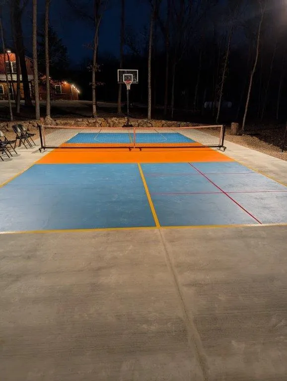 Full court at night with pickleball net, basketball hoop, and volleyball